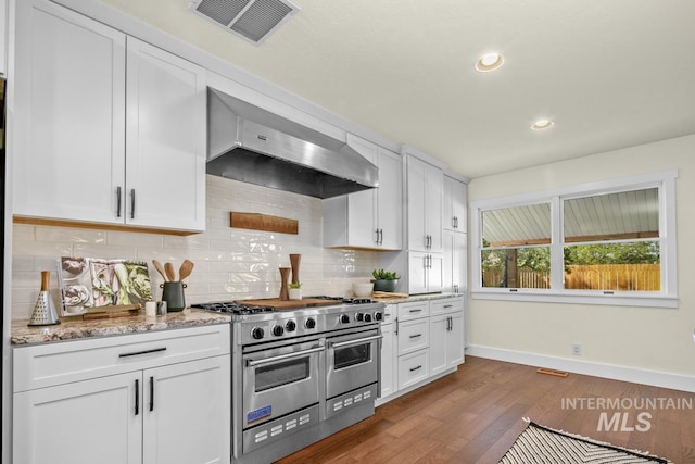 kitchen with range with two ovens, baseboards, visible vents, ventilation hood, and dark wood-type flooring