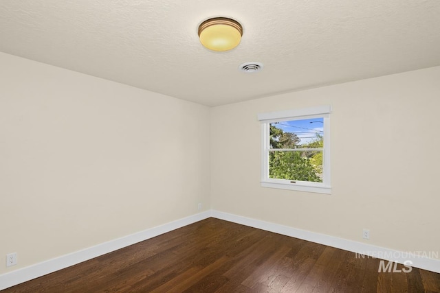 spare room with dark wood finished floors, visible vents, baseboards, and a textured ceiling