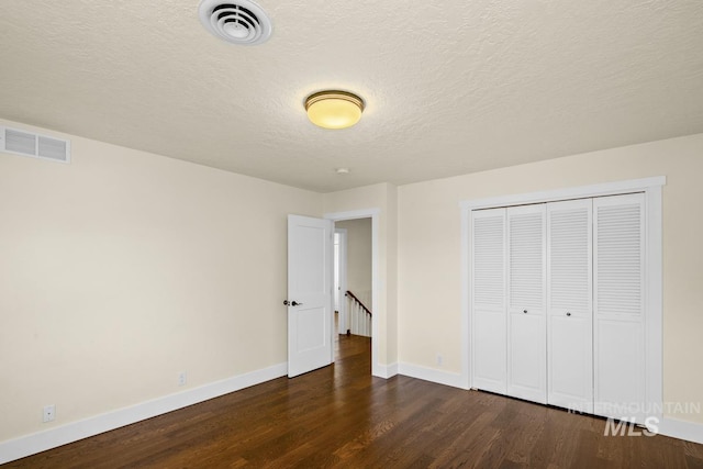 unfurnished bedroom with a textured ceiling, visible vents, baseboards, and dark wood-style floors