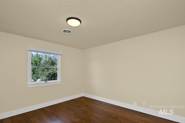 spare room with baseboards, a textured ceiling, visible vents, and dark wood-style floors