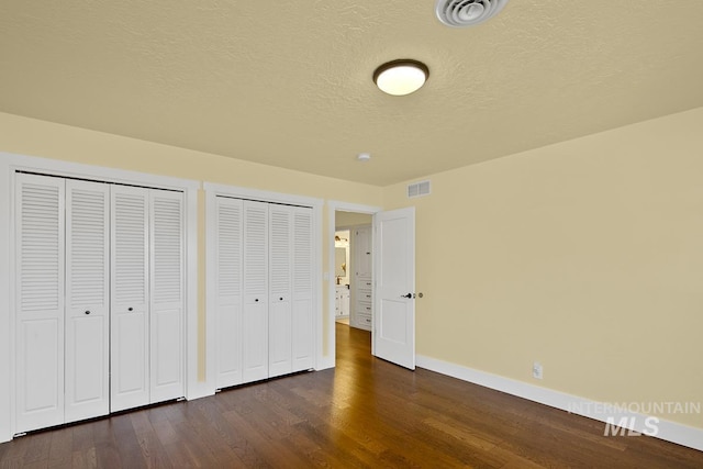 unfurnished bedroom with baseboards, visible vents, two closets, and dark wood-type flooring