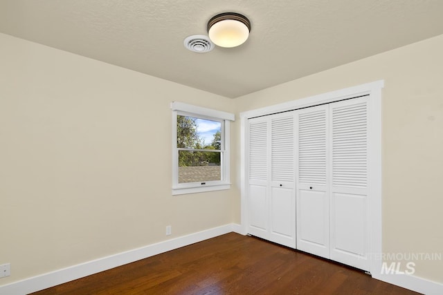unfurnished bedroom featuring baseboards, a closet, visible vents, and dark wood finished floors