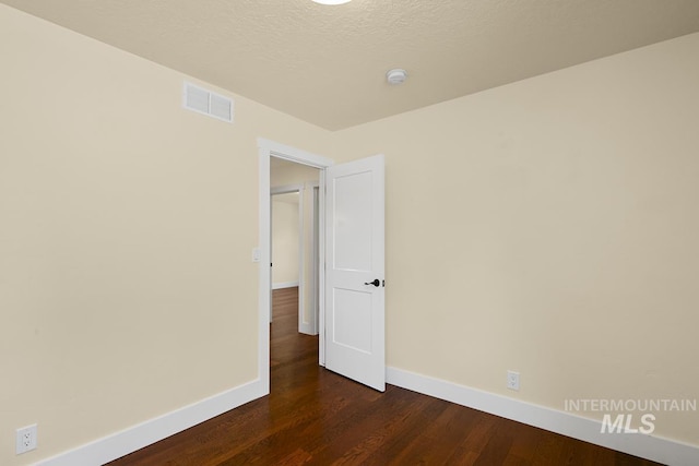 empty room with a textured ceiling, baseboards, visible vents, and dark wood finished floors