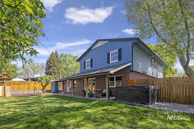 rear view of house with a patio, a playground, a lawn, a hot tub, and a fenced backyard