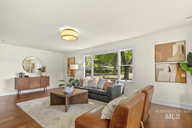 living room with a textured ceiling, dark wood-type flooring, and baseboards