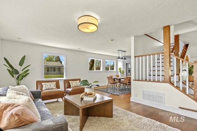 living area featuring baseboards, stairs, visible vents, and wood finished floors