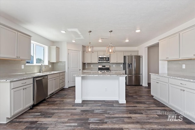 kitchen featuring dark hardwood / wood-style floors, decorative backsplash, appliances with stainless steel finishes, decorative light fixtures, and a kitchen island