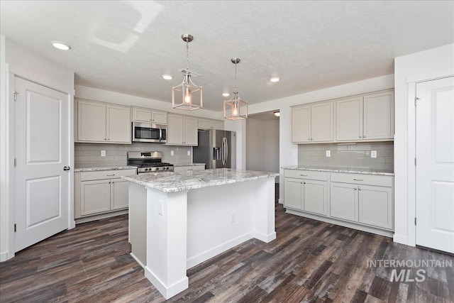 kitchen featuring dark hardwood / wood-style flooring, light stone counters, stainless steel appliances, pendant lighting, and a kitchen island