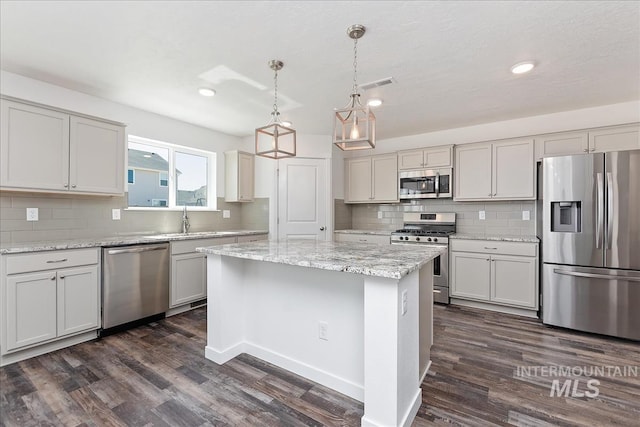 kitchen with sink, a center island, dark wood-type flooring, decorative light fixtures, and appliances with stainless steel finishes