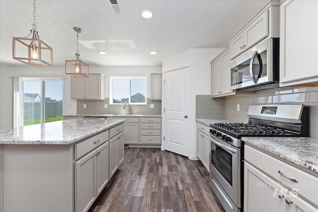 kitchen featuring sink, dark hardwood / wood-style flooring, pendant lighting, a kitchen island, and appliances with stainless steel finishes