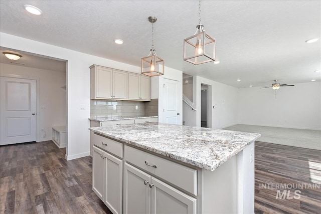 kitchen featuring ceiling fan, dark wood-type flooring, hanging light fixtures, decorative backsplash, and a kitchen island