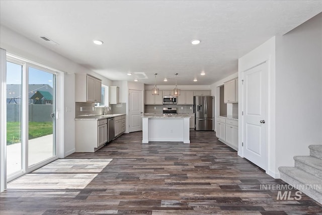 kitchen with dark hardwood / wood-style flooring, backsplash, stainless steel appliances, pendant lighting, and a kitchen island