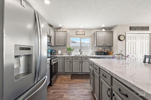 kitchen featuring a sink, stainless steel appliances, gray cabinetry, and dark wood-style flooring