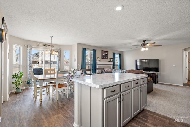 kitchen with gray cabinetry, a kitchen island, open floor plan, light countertops, and dark wood-style floors