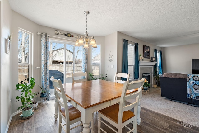 dining space featuring a chandelier, a textured ceiling, a lit fireplace, and wood finished floors