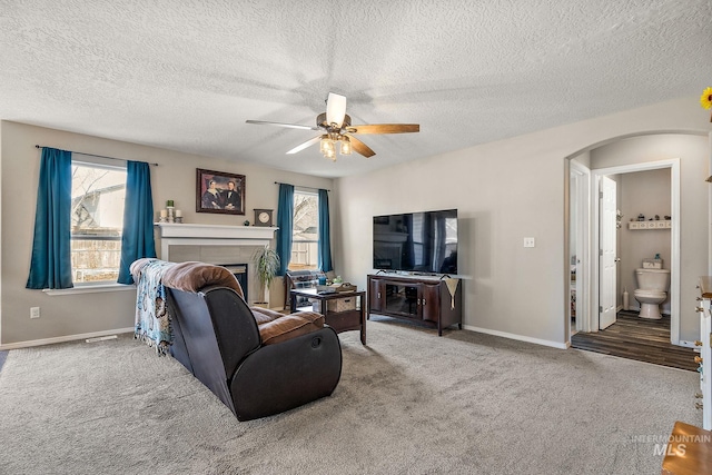 carpeted living room with arched walkways, a fireplace, baseboards, and a ceiling fan