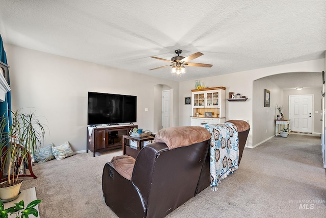 living room featuring a textured ceiling, arched walkways, baseboards, light colored carpet, and ceiling fan