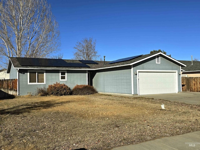 ranch-style home featuring a garage, driveway, fence, and roof mounted solar panels