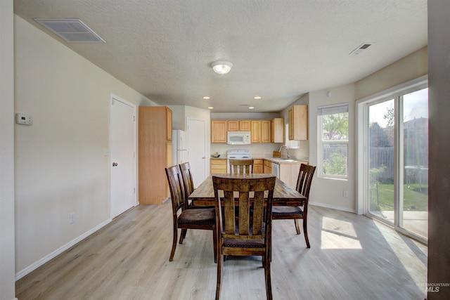 dining area featuring baseboards, visible vents, light wood-style floors, and a textured ceiling