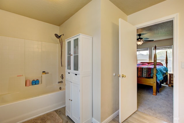 bathroom with a textured ceiling,  shower combination, wood finished floors, and ensuite bathroom