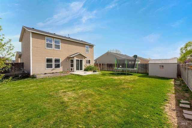 back of house featuring a trampoline, an outdoor structure, a fenced backyard, a storage unit, and a patio