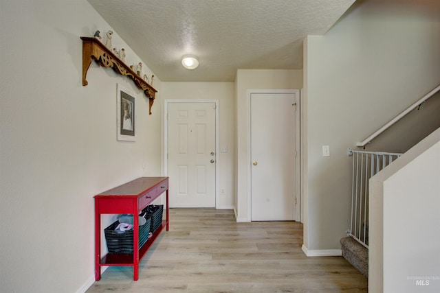 entryway with baseboards, a textured ceiling, and light wood-style flooring