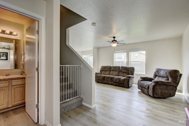 living area featuring a textured ceiling, ceiling fan, light wood-type flooring, and baseboards