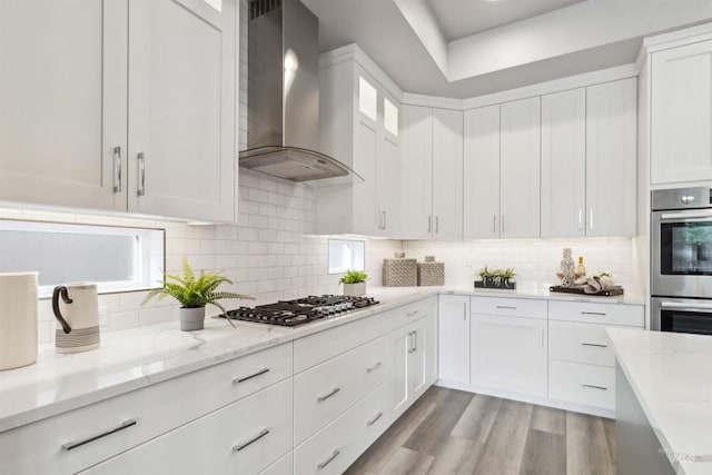 kitchen with appliances with stainless steel finishes, white cabinetry, decorative backsplash, and wall chimney exhaust hood