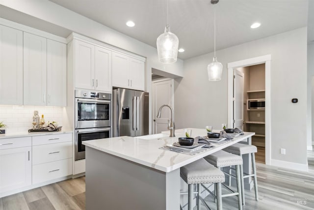 kitchen with light stone countertops, appliances with stainless steel finishes, a kitchen island with sink, and white cabinetry