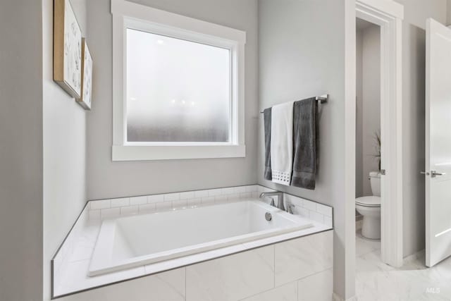 bathroom featuring toilet, tiled bath, and a healthy amount of sunlight