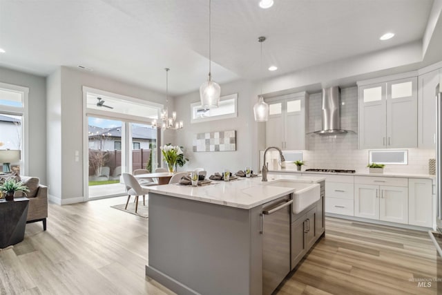 kitchen with sink, white cabinetry, wall chimney exhaust hood, stainless steel dishwasher, and hanging light fixtures