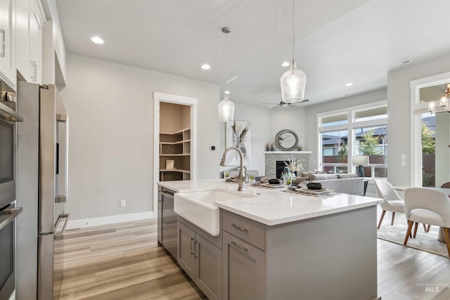 kitchen featuring sink, pendant lighting, light stone countertops, a kitchen island with sink, and a stone fireplace