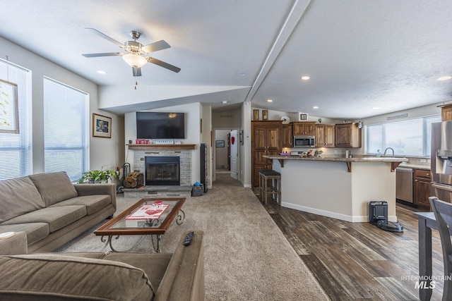 living area featuring lofted ceiling, a textured ceiling, a stone fireplace, baseboards, and dark wood-style floors