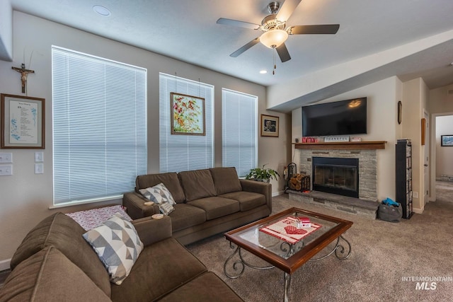 living room featuring carpet floors, a stone fireplace, baseboards, and a ceiling fan