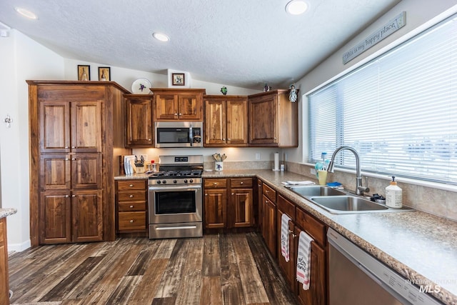 kitchen with appliances with stainless steel finishes, dark wood-type flooring, vaulted ceiling, a textured ceiling, and a sink