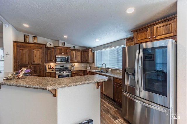 kitchen with stainless steel appliances, dark wood-type flooring, vaulted ceiling, a sink, and a kitchen bar