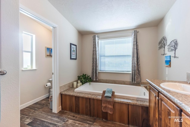 full bath featuring baseboards, wood finished floors, a textured ceiling, vanity, and a bath