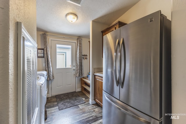 kitchen featuring brown cabinetry, washing machine and clothes dryer, dark wood finished floors, and freestanding refrigerator