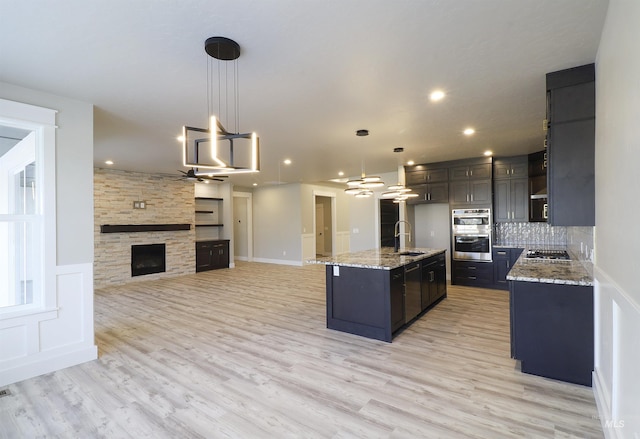 kitchen with hanging light fixtures, a stone fireplace, sink, and a center island with sink