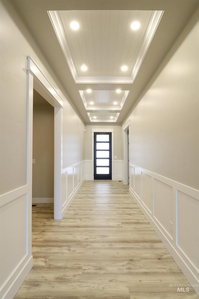 hallway with a raised ceiling, ornamental molding, and light hardwood / wood-style floors