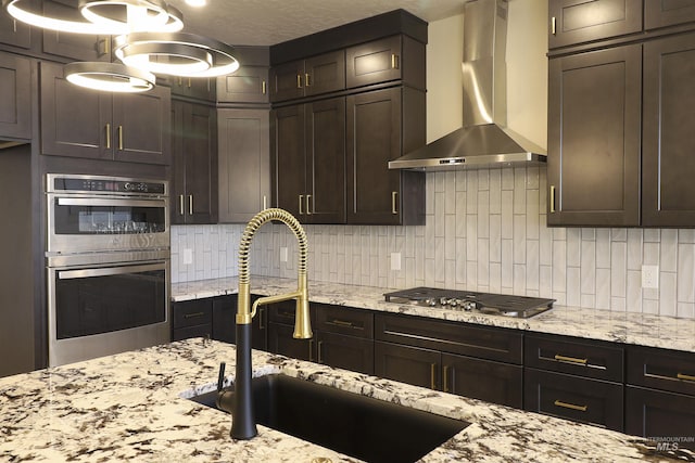 kitchen with tasteful backsplash, sink, light stone counters, stainless steel appliances, and wall chimney exhaust hood