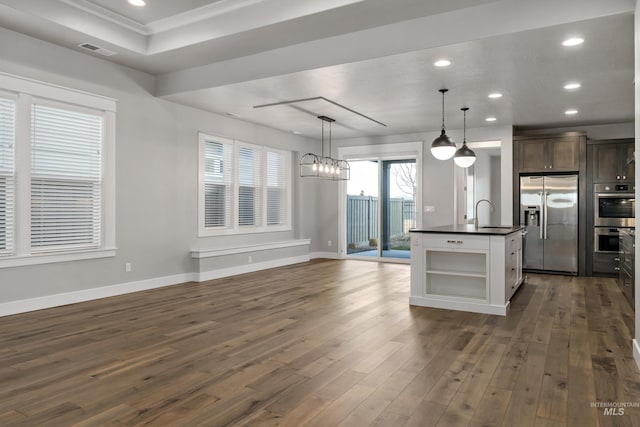 kitchen featuring dark brown cabinets, dark hardwood / wood-style floors, an island with sink, pendant lighting, and stainless steel appliances