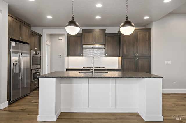 kitchen featuring appliances with stainless steel finishes, dark brown cabinetry, a center island with sink, dark hardwood / wood-style flooring, and decorative light fixtures