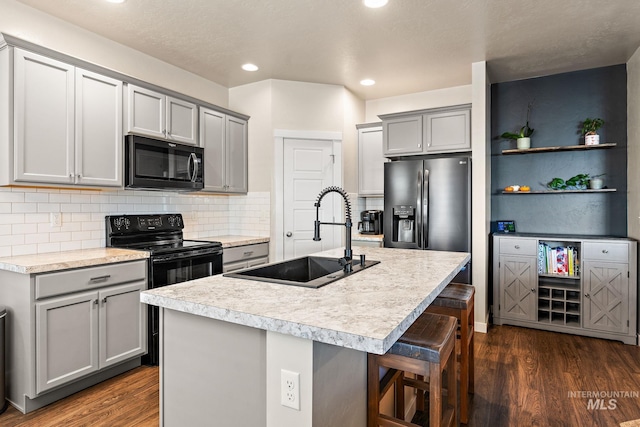 kitchen featuring gray cabinets, a breakfast bar area, an island with sink, stainless steel fridge, and sink