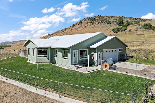 single story home with a garage, a mountain view, central AC unit, and a front lawn