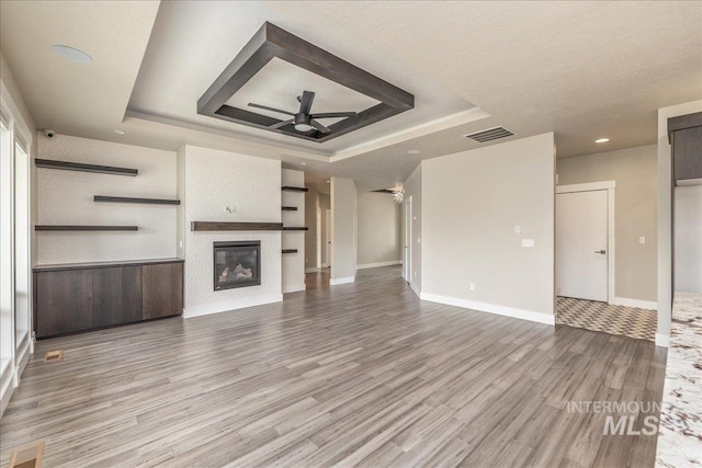 unfurnished living room featuring a tray ceiling, a ceiling fan, visible vents, and light wood finished floors