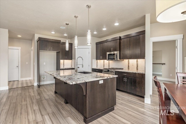 kitchen featuring a sink, a kitchen breakfast bar, backsplash, stainless steel appliances, and dark brown cabinets