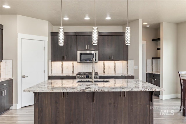 kitchen with stainless steel microwave, backsplash, dark brown cabinets, and light wood finished floors