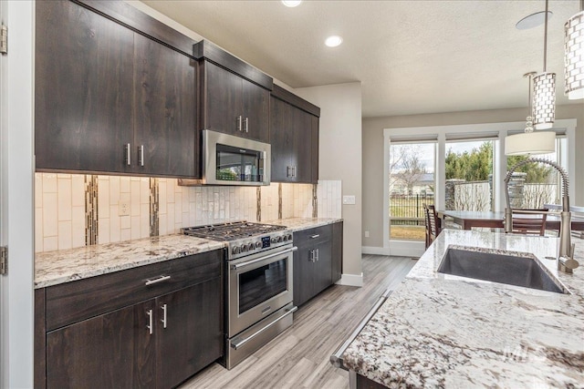 kitchen featuring tasteful backsplash, light stone countertops, light wood-style floors, stainless steel appliances, and a sink