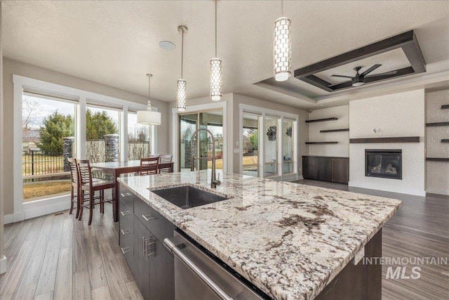 kitchen featuring a ceiling fan, light wood finished floors, a tray ceiling, a sink, and dishwasher